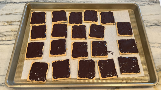 Add chocolate to crackers: Using about 1 heaping teaspoon per cracker, spread melted chocolate evenly to each corner. The chocolate will begin to harden as you work.