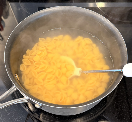 When the water reaches a boil, reduce heat to medium low and add the Banza shells. Stir occasionally and cook 9 to 11 minutes. The water will turn a milky white.