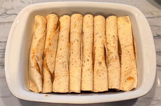Lay out the tortillas and spread 2 Tbsp. of the enchilada mixture on each one. Wrap each tortilla around a hot dog and place it seam side down in the baking dish, on top of the beans.