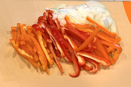 While the casserole bakes, cut the onion and bell peppers into slices. Then heat the olive oil in a lidded pan over medium heat. Sauté the onion and bell peppers for about 6 minutes.
