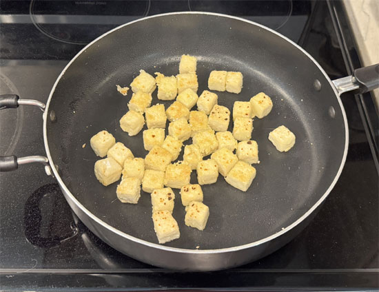 Heat a large skillet over medium-high heat. Add the olive oil and then the tofu cubes. Cook until one side is golden brown and crisp, about 3 minutes. Flip and cook on the other side for three more minutes until the tofu is golden brown and crisp. Transfer the cooked tofu to a plate.