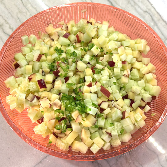 Cut a serrano pepper in half, remove the seeds, and mince them into small pieces. Then, put that in with the apples and cucumbers.