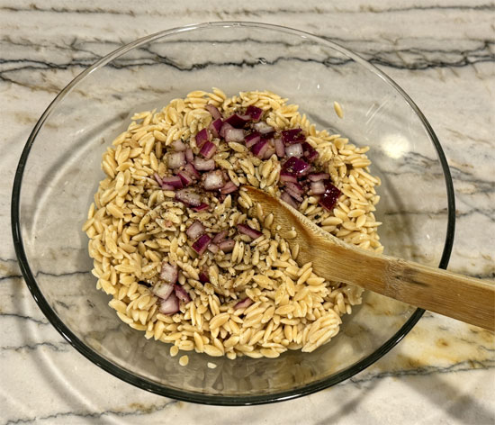 Pour half the dressing over the hot orzo. Add chickpeas, tomatoes, and olives. Toss well.