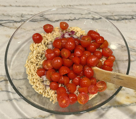 Pour half the dressing over the hot orzo. Add chickpeas, tomatoes, and olives. Toss well.